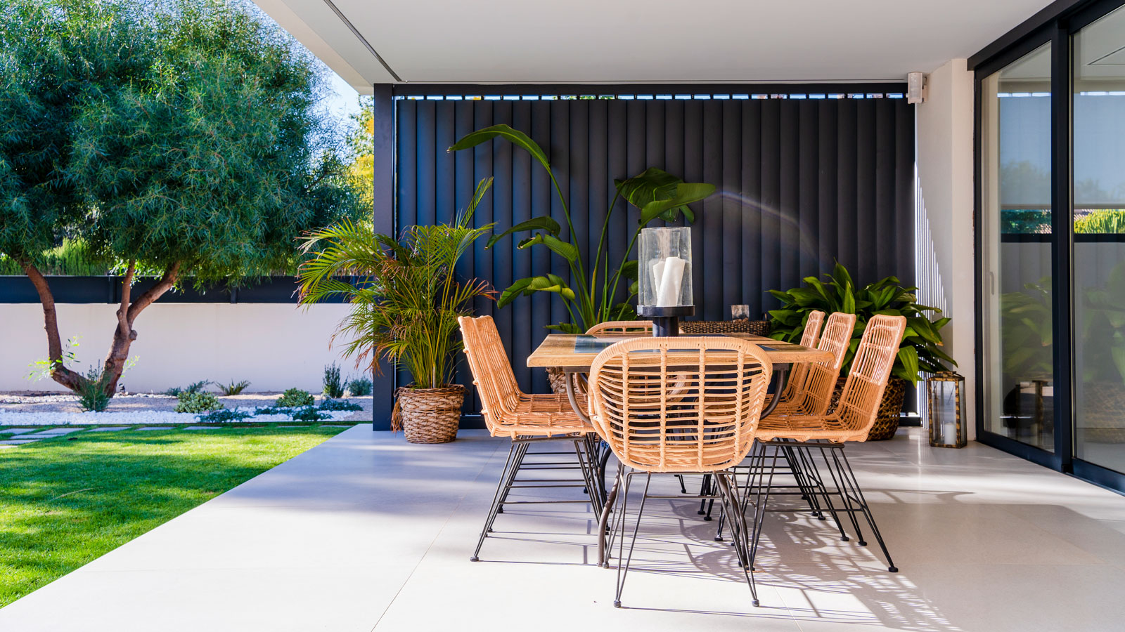 modern patio area with pavers, outdoor dining set and potted plants, and a tree and lawn beyond