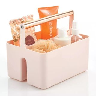 A pink storage basket with a rose gold handle and products