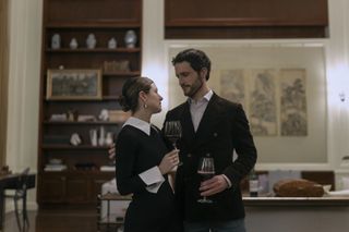 Elise Kibler as Sloane and Rob Heaps as Tomas Bal embracing and holding wine glasses in a home in a still from the night agent season 2