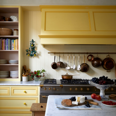 Kitchen with yellow units, cream walls, parquet flooring and large range cooker with saucepans hanging on the wall above. 