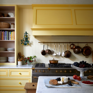 Kitchen with yellow units, cream walls, parquet flooring and large range cooker with saucepans hanging on the wall above.