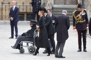 India Hicks wearing a black hat and dress pushing her mother Lady Pamela Mountbatten in a wheelchair at Queen Elizabeth's funeral