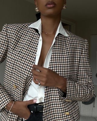 Model Jasmine Tookes wears checkered blazer, white button down, and black jeans while posing in tennis bracelet.