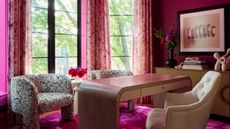 home office with magenta carpets and walls, patterned armchairs, a curved timber desk, and console table with artwork hanging above