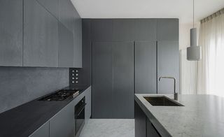 The cabinets and counters of the kitchen are dark gray and there is a marble counter top in the middle