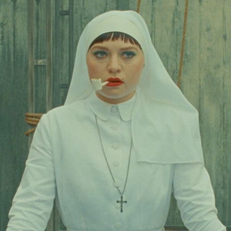 mia threapleton as a nun in a white habit smoking a pipe in the phoenician scheme