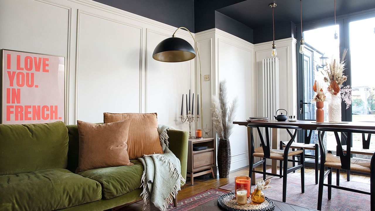 white living room diner with black ceiling, wall panelling, green velvet sofa, black arc lamp, dining table, wishbone chairs, wood flooring