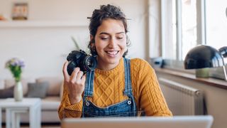 Female photographer holding camera inside home office and smiling