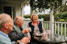 A group of seniors smile on a porch. There's a view of a garden beyond.