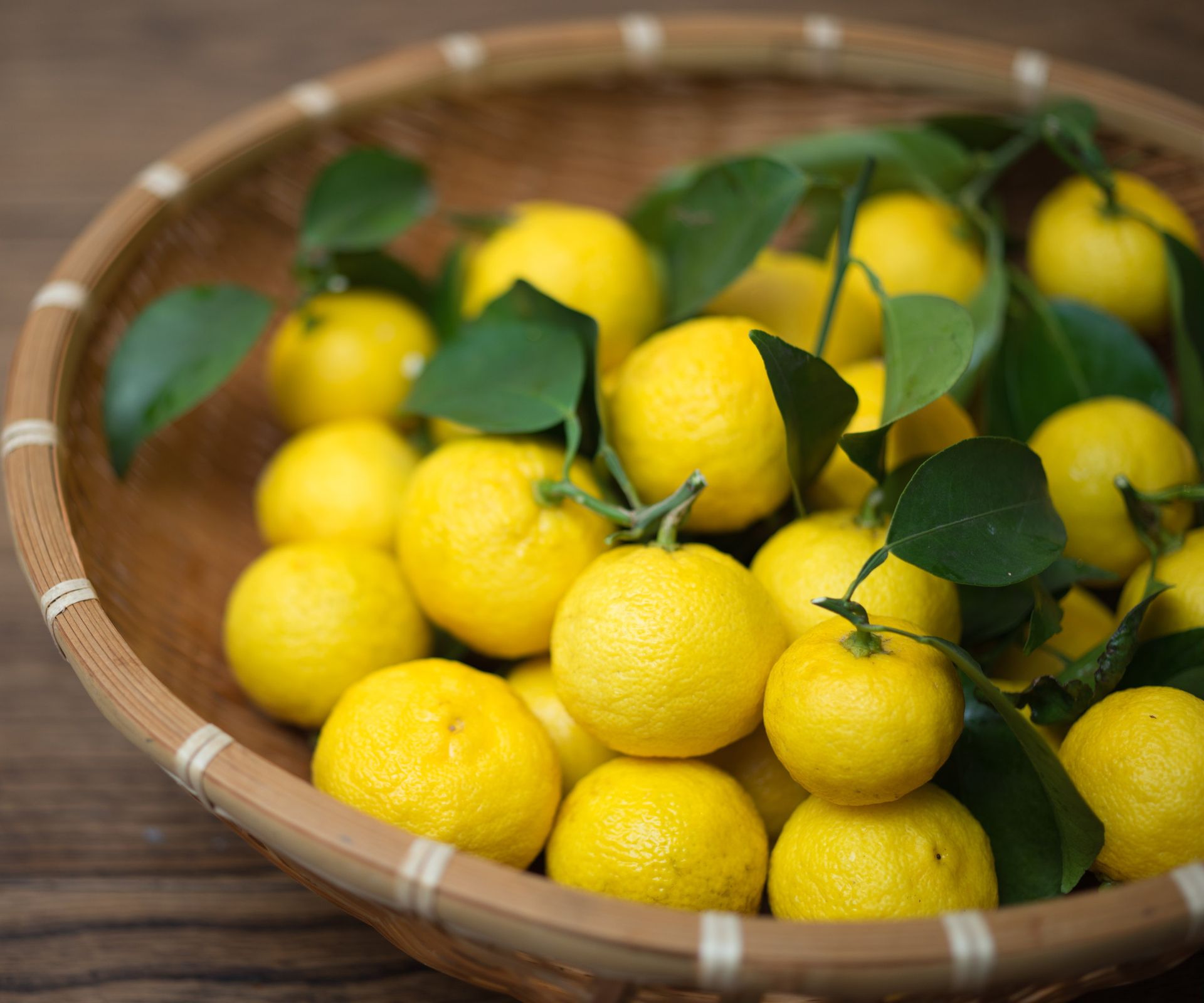 Yellow yuzu fruits displayed in a bamboo basket on a wooden table