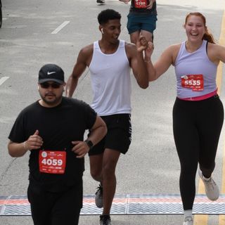 Emery Little runs the Life Time half marathon in Chicago. She is running with a friend, her hair tied back and a fitness tracker on her wrist. In the background we see other runners and crowds lining the street.