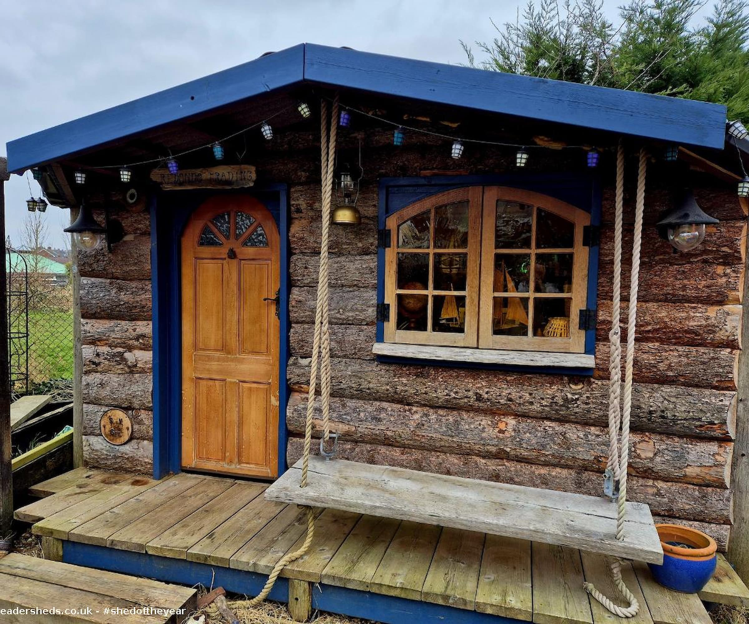 A log cabin shed with swing chair and blue balustrades and small step