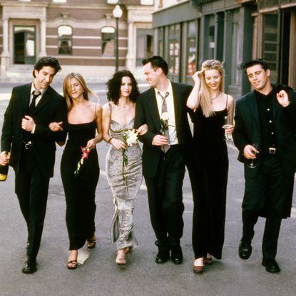 The cast of Friends walking down a NYC street in black dresses and suits