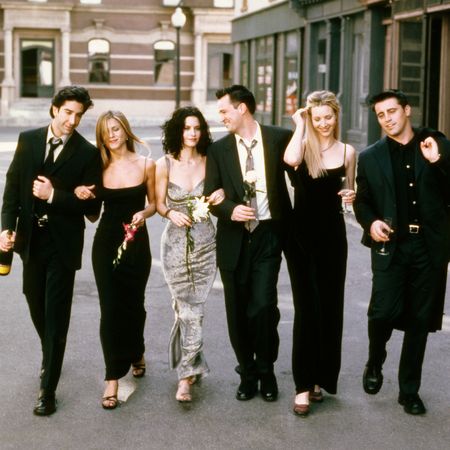 The cast of Friends walking down a NYC street in black dresses and suits