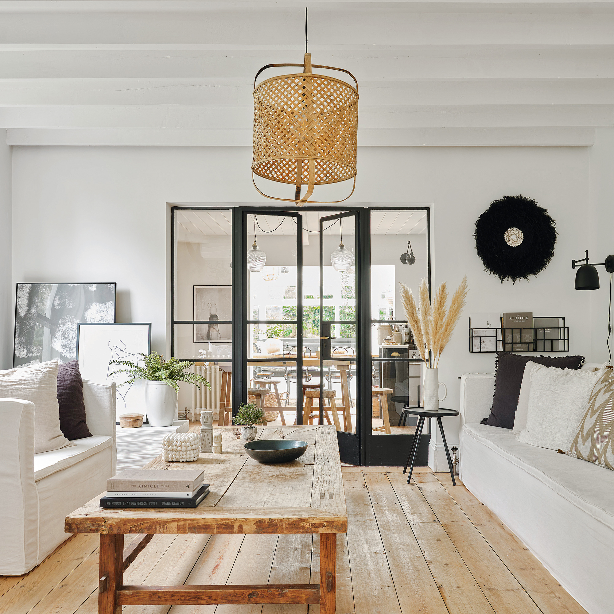 a white living room with two white sofas, wooden flooring and a wooden dining table and Crittal internal doors leading into another room