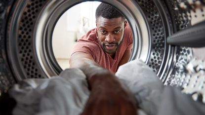 Best washing machine, image shows man placing clothes inside front loading washing machine