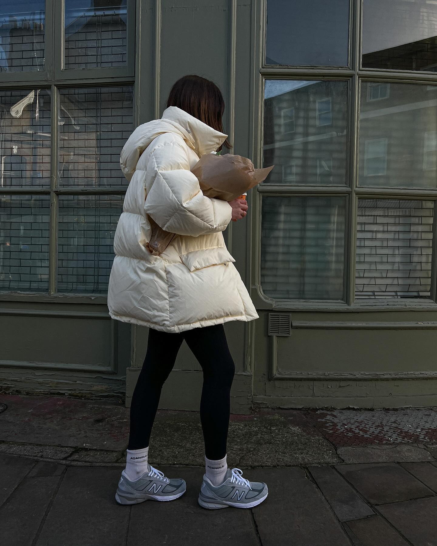 Fashion person francescasaffari wears a trending trainer brand 2026. She wears grey New Balance trainers. She wears them with black leggings and a butter yellow puffer jacket. This image was recently taken from her Instagram.