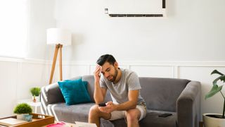 Man sweating on the sofa with AC unit behind him