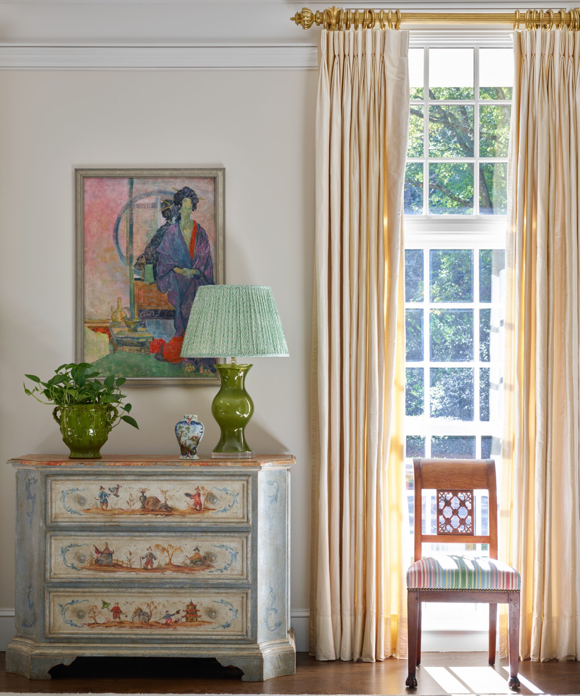 Hallway with long window and drapes, antique painted dresser, green lamp and vase and antique painting