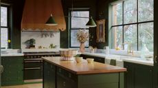 dark green kitchen with wooden countertop and wooden scalloped range cooker hood with large windows and green pendant light
