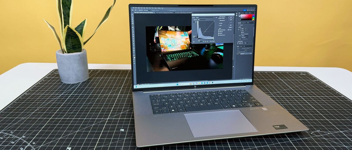 HP ZBook Studio 16 G11 mobile workstation on a white desk with a black table mat, against a yellow backdrop.