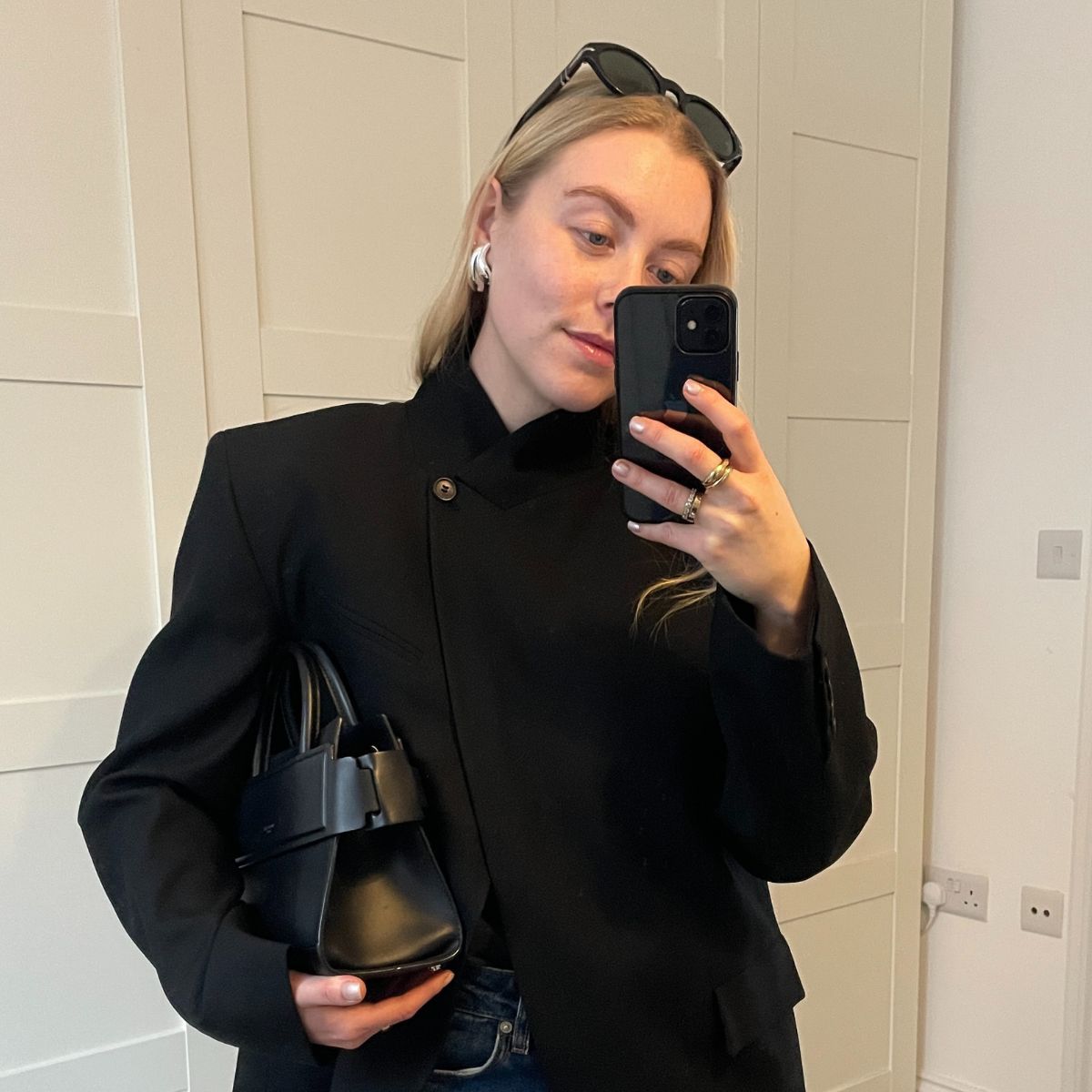 Woman wears high neck black blazer, carries black bag