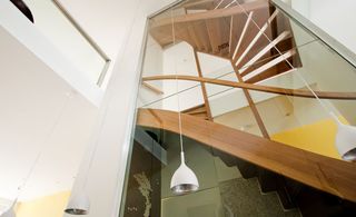 View of the wooden stairs on different floors captured from the bottom up. White ceiling pendant lighting.