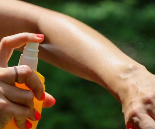 spraying mosquito spray on arm
