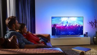 Bedste priser og tilbud på 4K TV: Et par sidder og ser en koncert på et Philips Ambilight TV