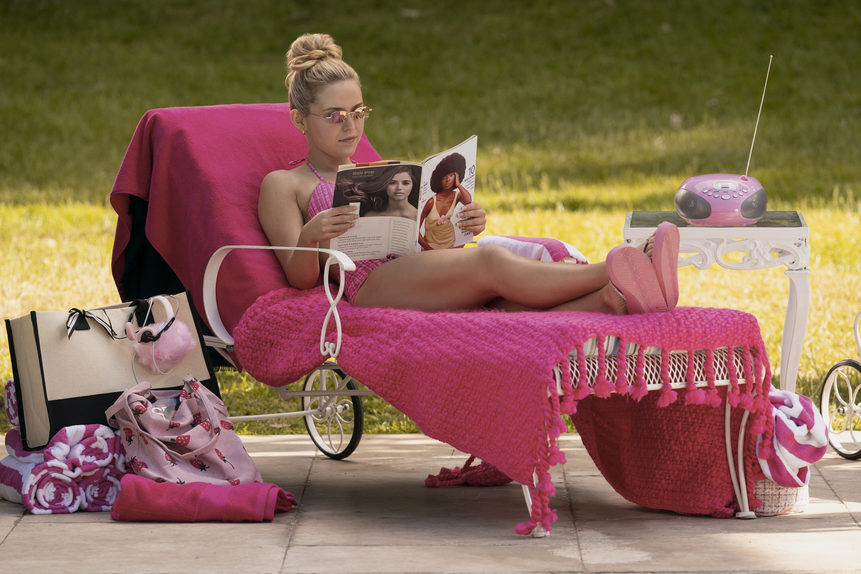 Lexi Minetree as elle woods lying on a lawn chair with a pink blanket on top reading a magazine in a still from elle