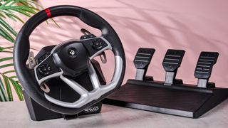 Hori Force Feedback Racing Wheel DLX on desk with plant and pink wall in background