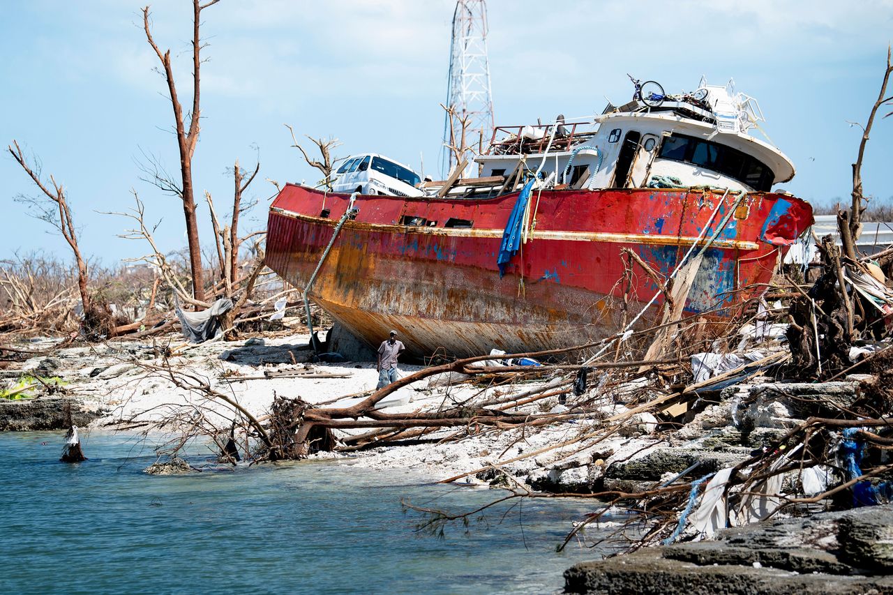 A damaged red boat sits on the shore among rubble