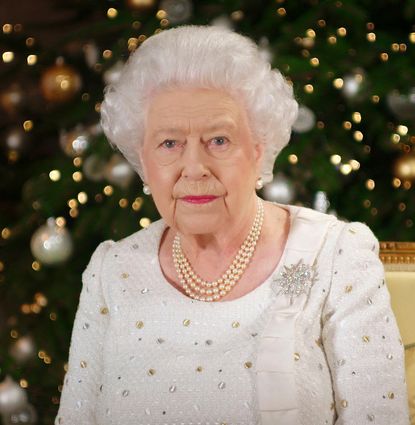 Queen Elizabeth wearing a white dress sitting in front of a Christmas tree