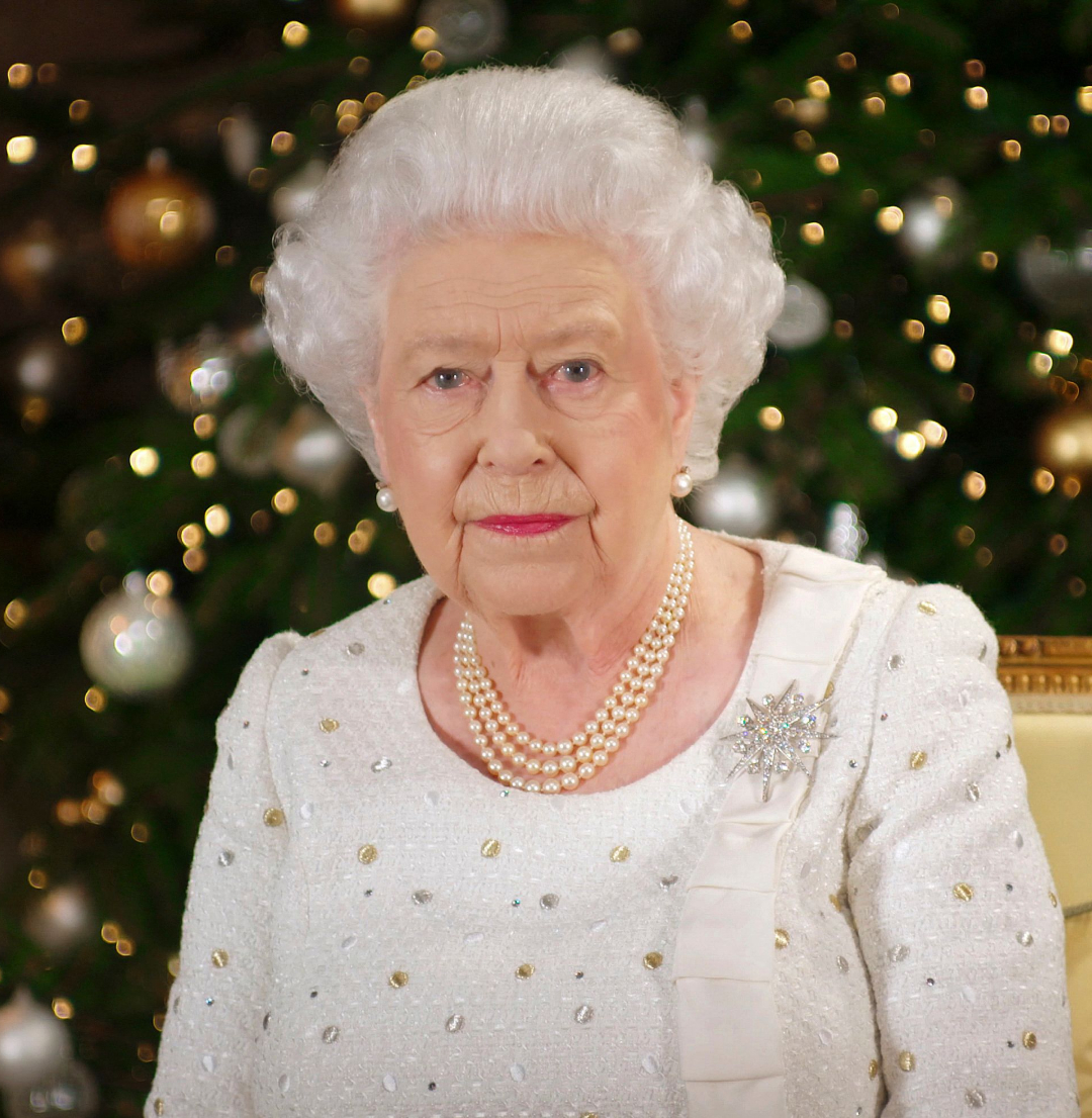 Queen Elizabeth wearing a white dress sitting in front of a Christmas tree