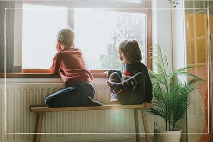 two small children sitting by a radiator and looking out of the window