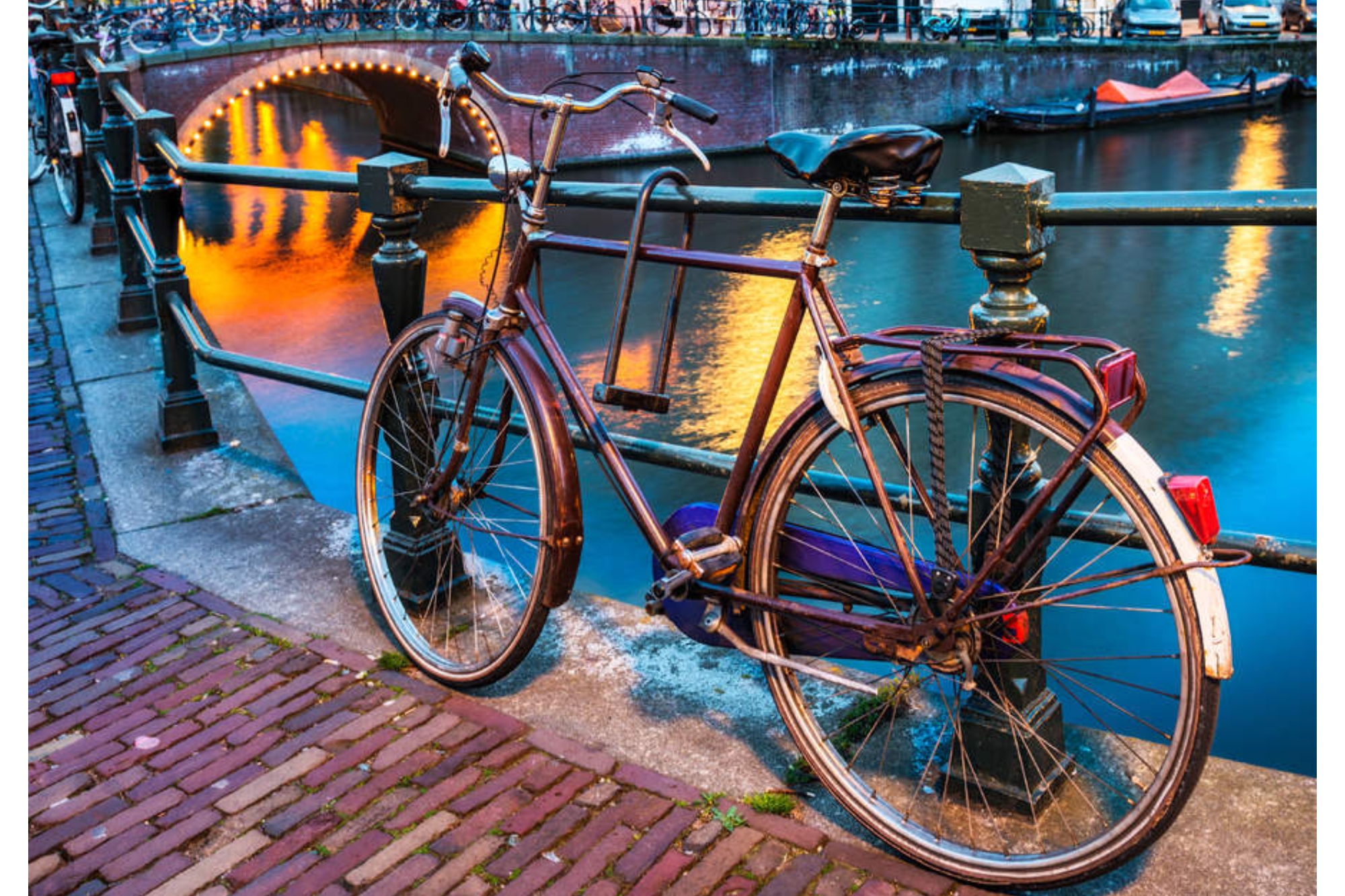 Dutch bikes can make the best commuter bikes for some. This image shows a bike at night lent up against railings with water behind it and a bridge illuminated in the background. The bike is pointing away from the viewer with the handlebars pointing left