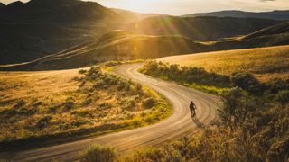 A cyclist rides down a gravel path under the sun