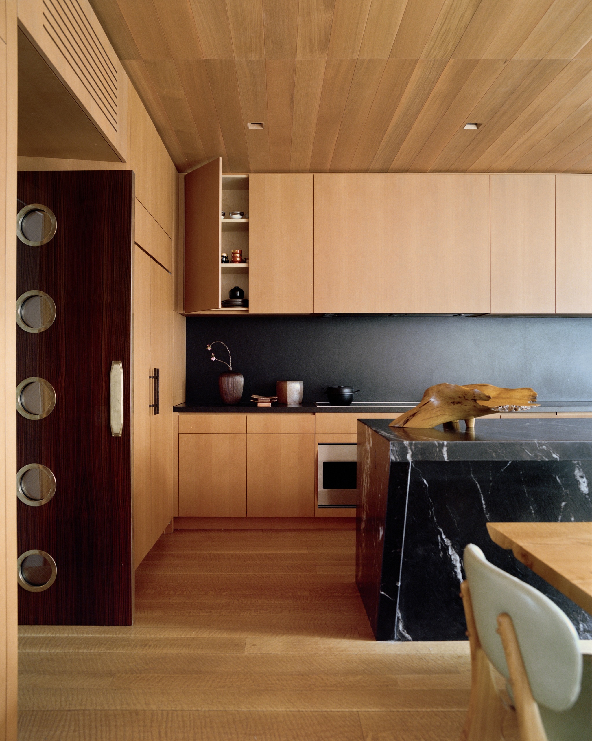 a wood kitchen with a black backsplash and black marble island