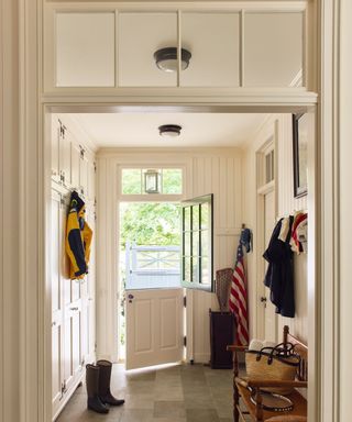 White hallway with wood panelling, dutch doors opening out onto garden, stone floor and coats hanging up