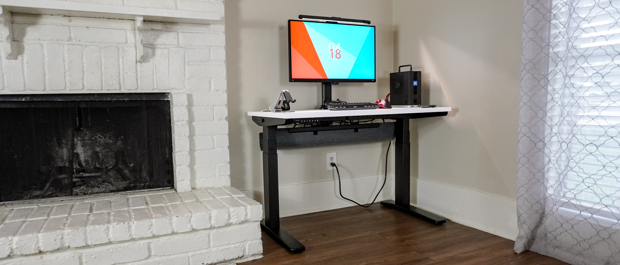 The Uplift V3 standing desk set up in a corner next to a fireplace