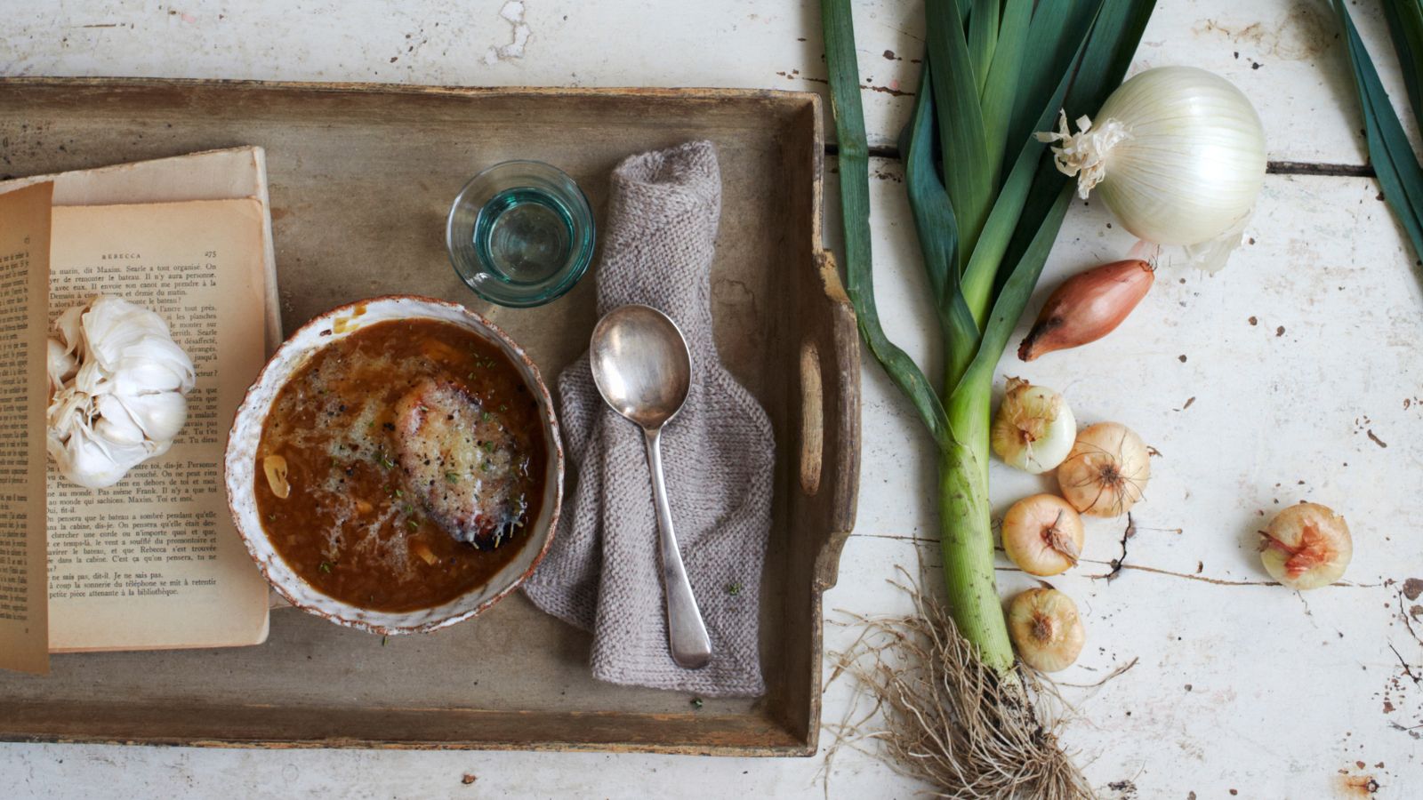 onion soup next to a leek, garlic bulb and onions on a wooden tray