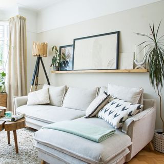 Neutral L-shaped sofa underneath floating shelf in beige living room