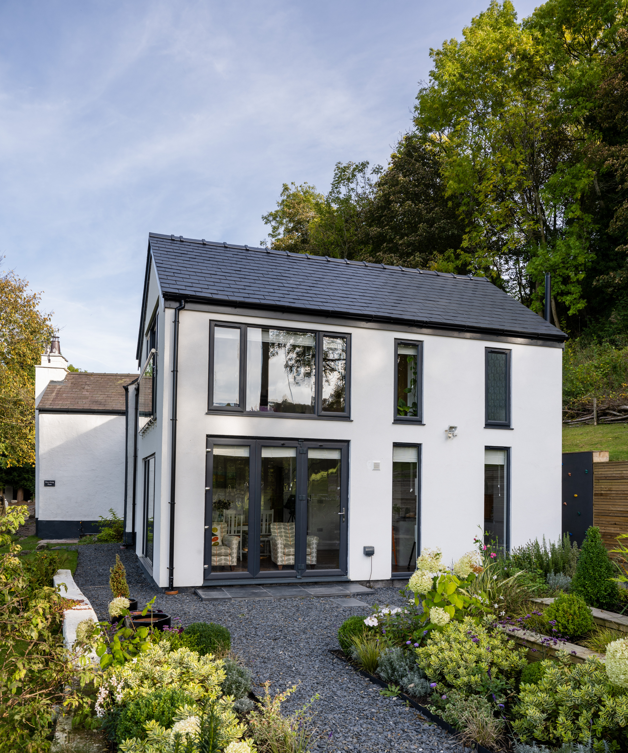 SIPs home with white render, grey aluminium framed windows and doors and grey slate roof