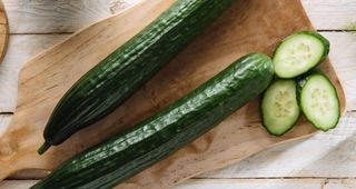 Cucumbers, whole and chopped, sitting on wooden chopping board