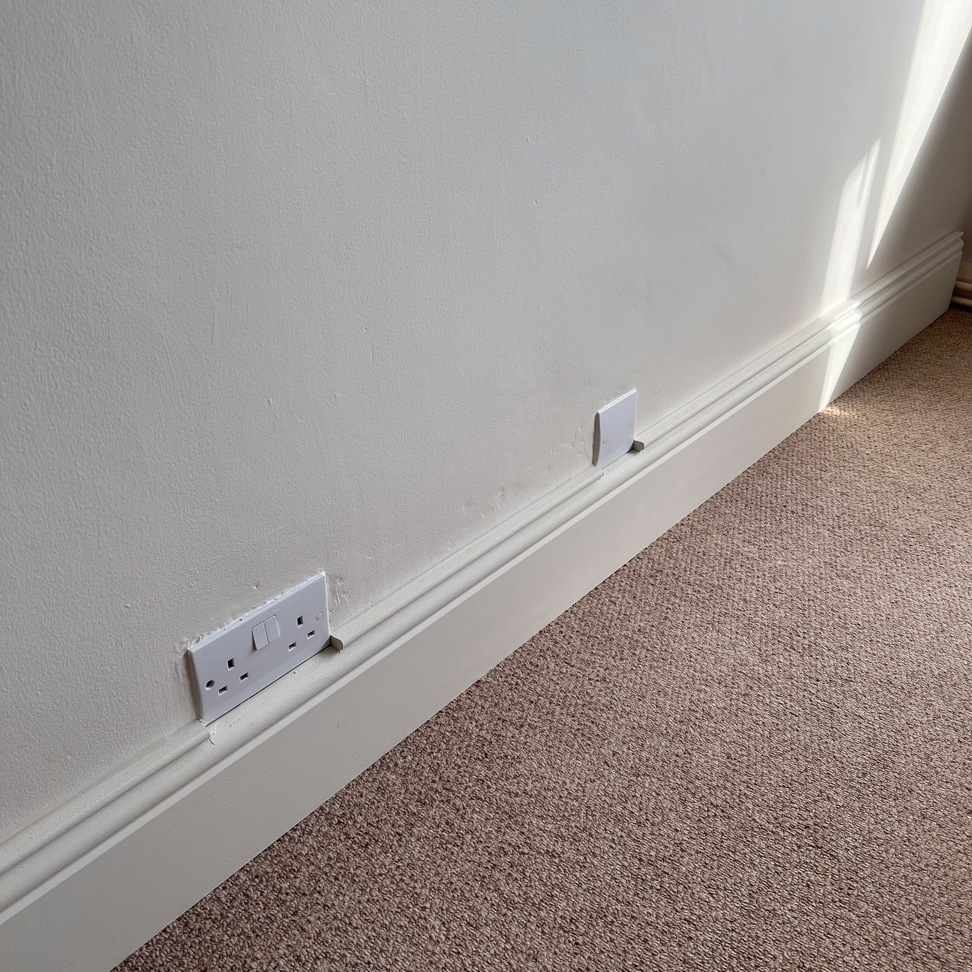 White wall with plugs by neutral carpet