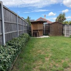 Lawn in garden surrounded by wooden fence and flower beds, with wooden garden bar and shed at end