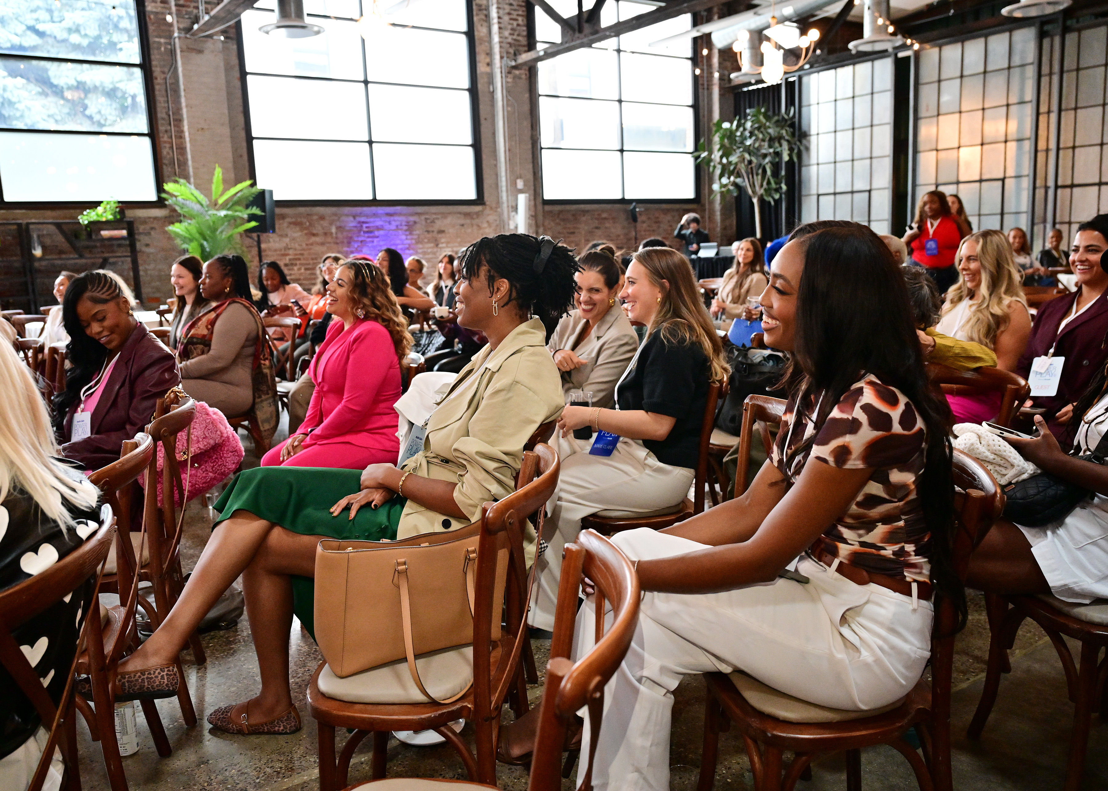 Audience members sit in rows of wooden chairs at Marie Claire&amp;rsquo;s Power Play summit in Philadelphia, laughing and smiling during a panel discussion inside a bright industrial loft space.