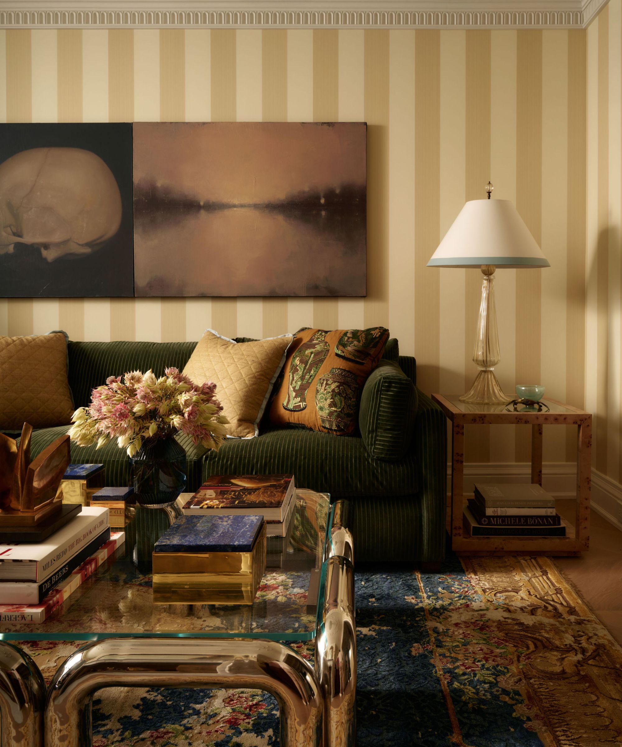 a large living room with yellow striped wallpaper, a large green couch, vintage rug, stainless steel coffee table and oversized art and lamps