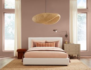 A bedroom with a double bed, a wicker lampshade and walls painted a dusky pink