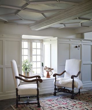 Gray panelled study with Tudor ceiling and white chairs in 12th century Cotswolds country house